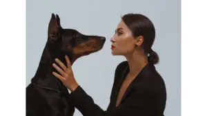 A stylish woman gazes at a Doberman in an intimate studio setting, creating a striking moment that perfectly captures the charm of pet lookalikes