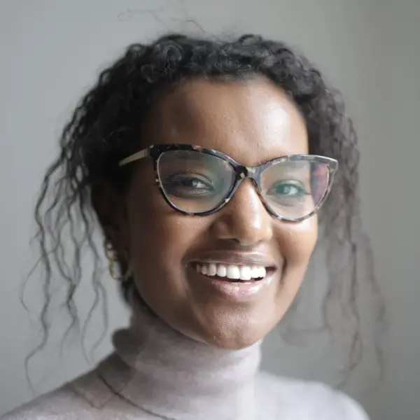 Smiling woman wearing glasses and a pullover in a calm indoor environment, showcasing natural frames that complement her relaxed, confident look.