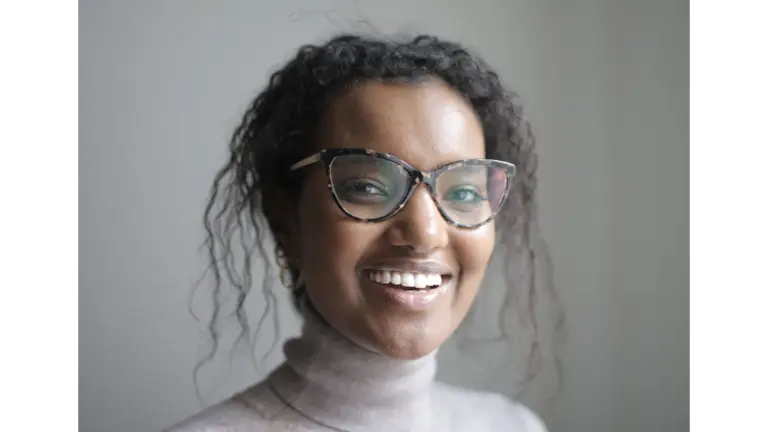 Smiling woman wearing glasses and a pullover in a calm indoor environment, showcasing natural frames that complement her relaxed, confident look.