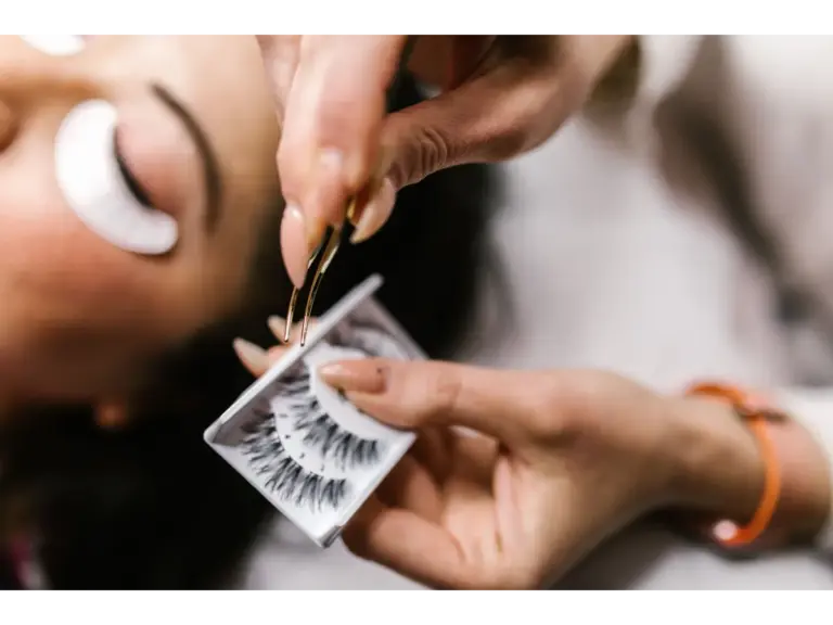 Close‑up of applying false eyelashes with tweezers during a beauty treatment, carefully blending them to enhance natural lashes.