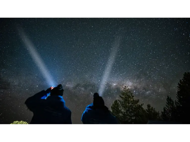 July stargazing glowing naturally in the moment, with two people with flashlights, under a starry night sky, surrounded by nature
