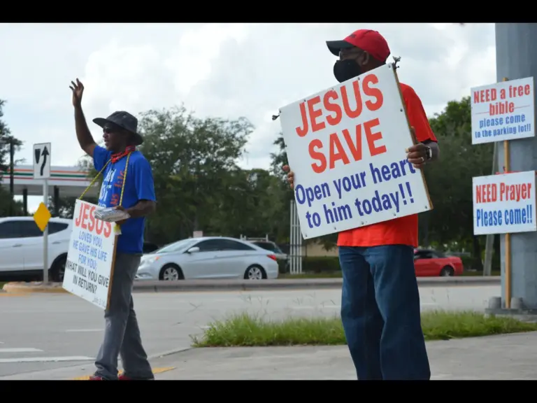 In daily devotional, an men in street ministry hold up signs to get sinners attention for their repentance.