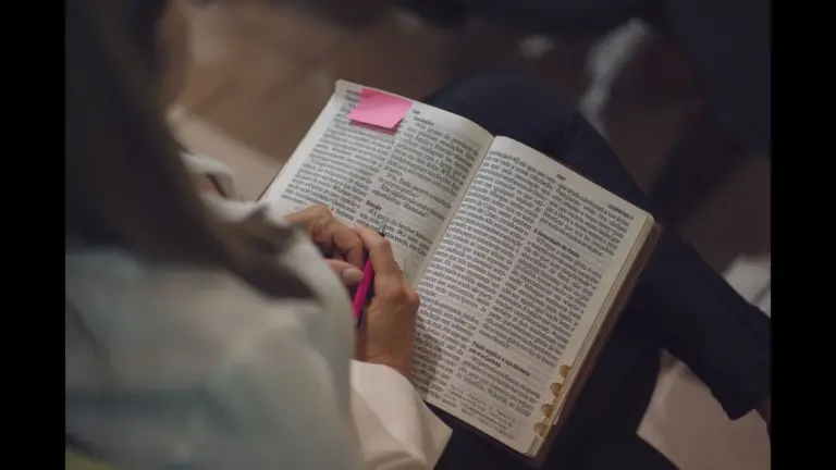 In Friday's daily devotional, a woman reads the Bible with a pink sticky note attached.