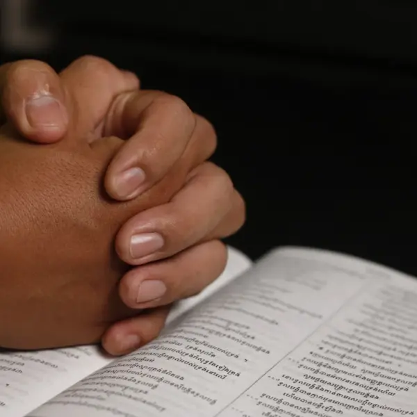 In Tuesday's daily devotional, a man's hands are folded in prayer on top of an open Bible.