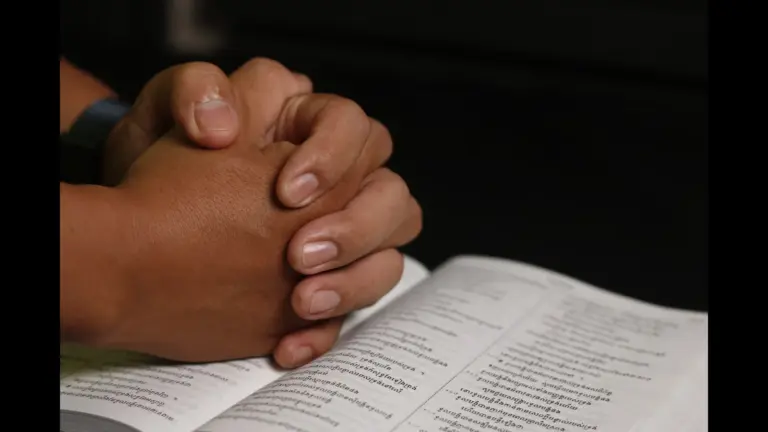 In Tuesday's daily devotional, a man's hands are folded in prayer on top of an open Bible.