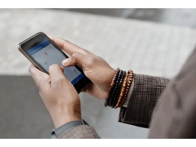 Close-up of hands with bracelets navigating on a smartphone using a GPS app outdoors, subtly reflecting how rising gas prices shape everyday travel choices.