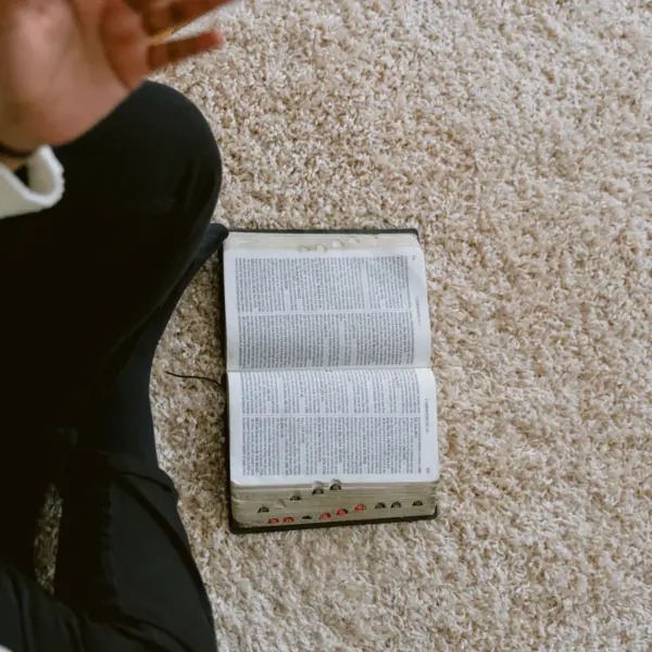 In daily devotional, a person sits on the floor with an open Bible, perhaps having Bible study.