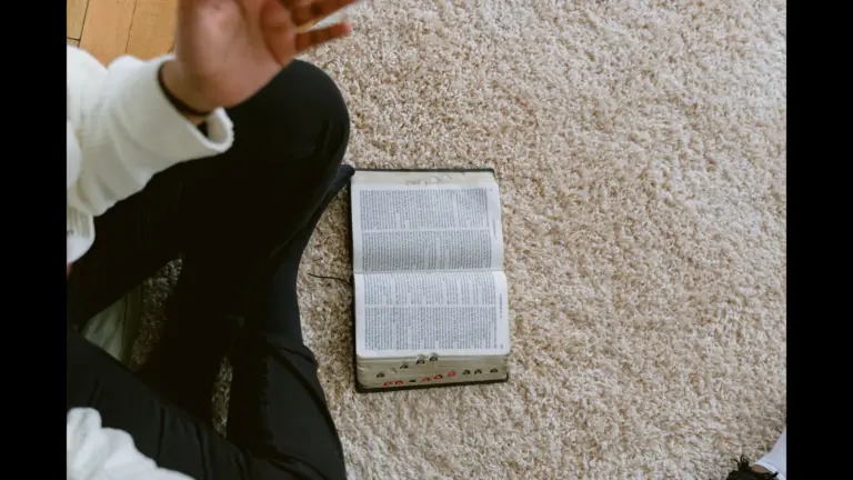 In daily devotional, a person sits on the floor with an open Bible, perhaps having Bible study.