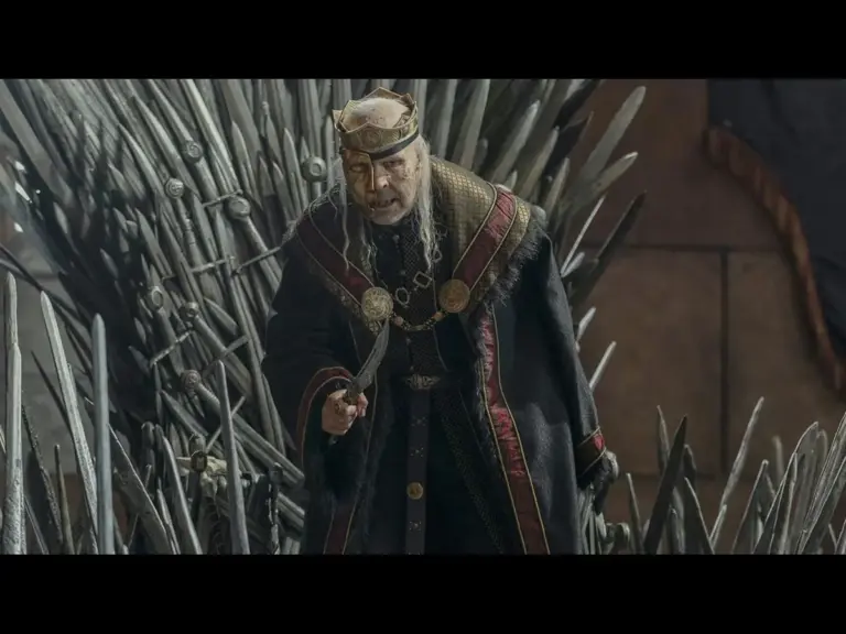 A man in a dark, ornate robe stands in front of a throne made of swords, holding a sword and appearing authoritative.