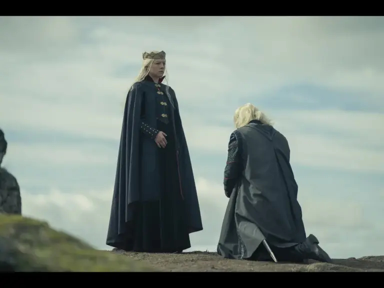 A regal figure in a crown stands on a rocky landscape while another figure kneels before them, with cloudy skies in the background.