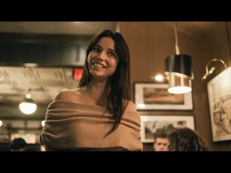 Inde Navarrette in Obsession (2025), in a cozy restaurant setting, smiling while wearing a stylish off-shoulder top.
