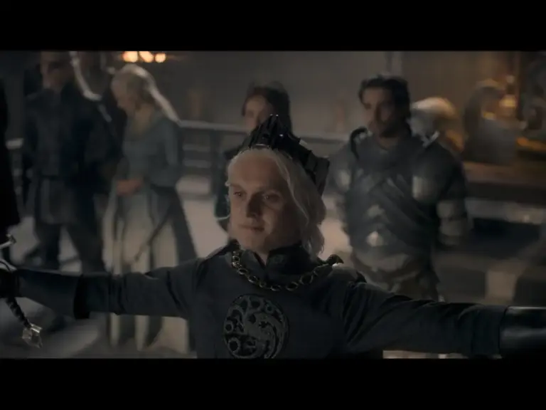 A character in a dark medieval outfit with a crown stands confidently, arms outstretched, in front of a group of individuals in a dimly lit setting.