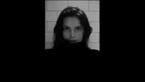 Inde Navarrette, dressed in a black sweater stands for a photo, displaying a cheerful expression and relaxed posture.