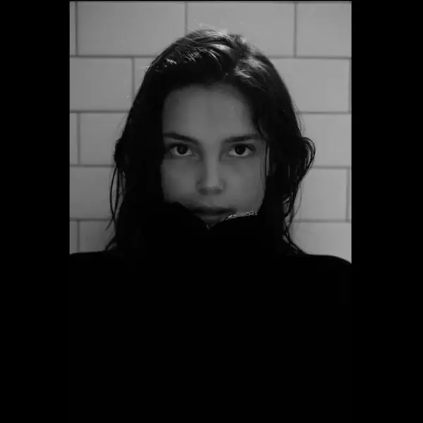Inde Navarrette, dressed in a black sweater stands for a photo, displaying a cheerful expression and relaxed posture.