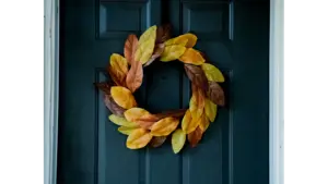 A fall wreath made of yellow, orange, and brown leaves hanging on a dark blue front door.