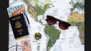 A flat lay of a world map featuring sunglasses, a U.S. passport, colorful push pins, some papers, and a ticket. Labor Day, vacation planning, trip planning, summer vacation