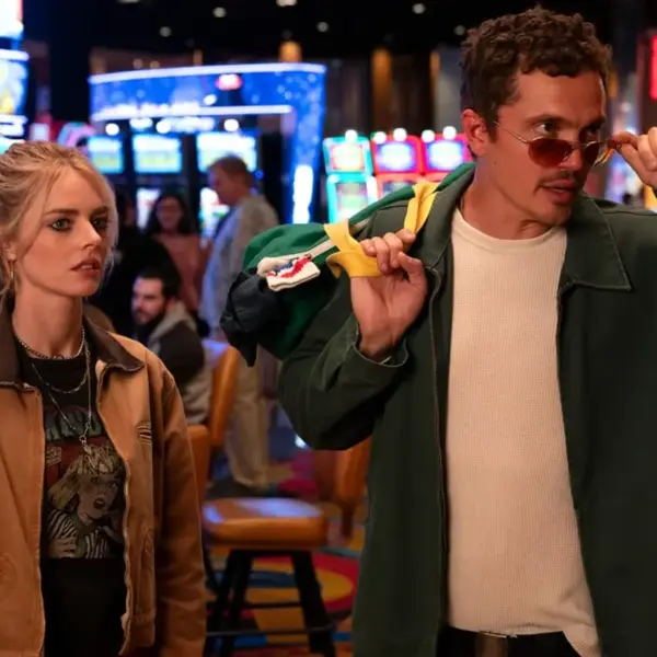 Samara Weaving and Karl Glusman are captured standing in front of a bustling casino, with colorful lights illuminating the scene in Eenie Meanie