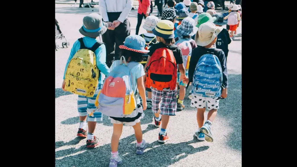 A group of children wearing colorful hats and backpacks walking away, with their backs turned to the camera. back to school, August