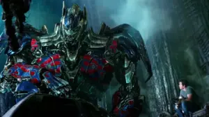 Peter Cullen portrayed Optimus Prime, with Mark Wahlberg from 2014 Transformers: Age of Extinction amid a dark and broken cityscape in the background