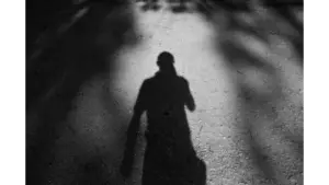 Black and white photo of a man's shadow on a textured, sunlit path outdoors, capturing the eerie presence of a ghost fugitive.