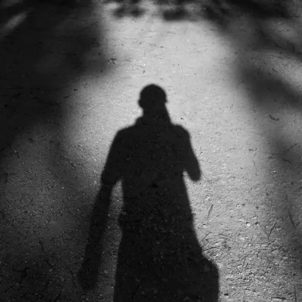 Black and white photo of a man's shadow on a textured, sunlit path outdoors, capturing the eerie presence of a ghost fugitive.