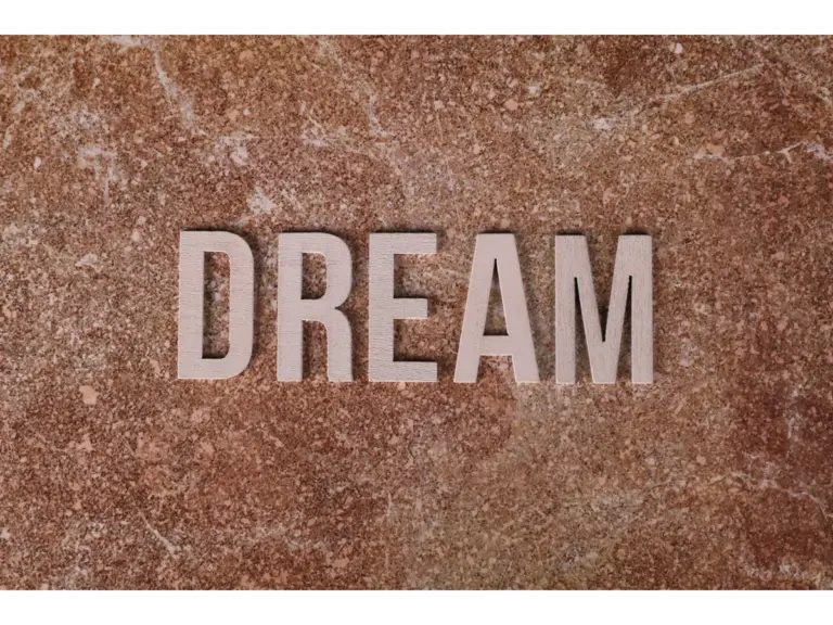 Dream symbolism appears in wooden letters spelling DREAM on a textured marble background, creating a soft, motivational aesthetic.