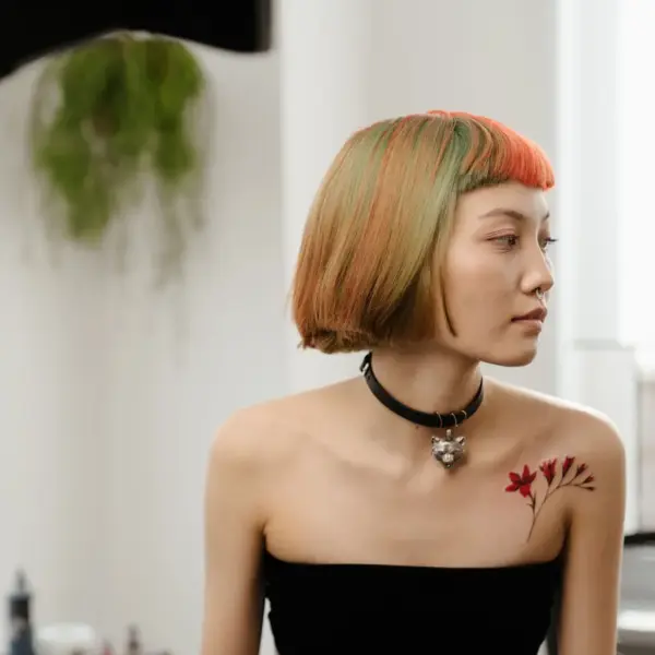 Stylish woman with colorful bob haircut and shoulder tattoo sits in a bright room, embodying the soft girl aesthetic with modern flair.