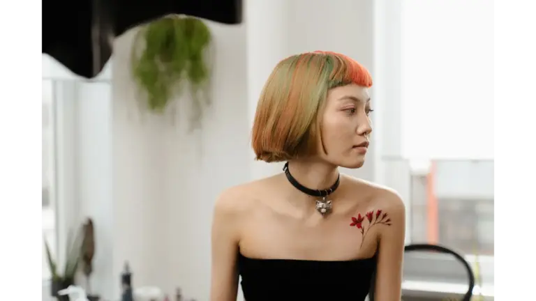 Stylish woman with colorful bob haircut and shoulder tattoo sits in a bright room, embodying the soft girl aesthetic with modern flair.