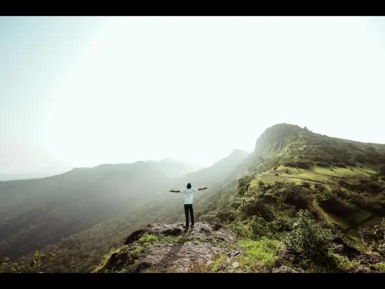 In Monday's daily devotional, a man stands amid a mountain with his arms outstretched to a loving God. 