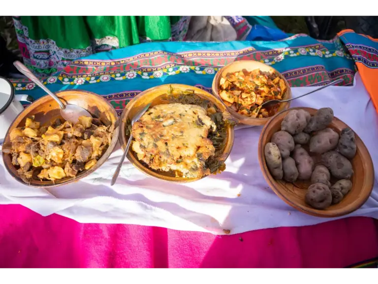 Traditional Andean ancient food displayed in wooden bowls, featuring potatoes, meat, and vegetable dishes on colorful woven fabric.