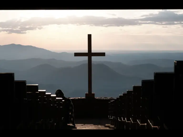 In Monday's daily devotional, a cross is seen at the end in the middle of two rows of seats at the front of an open buildling or sanctuary.