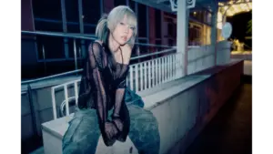 Woman sitting on a concrete ledge at night wearing a black mesh top and camo pants, styled with cool-toned lighting that reflects the Glam Guitar Trend aesthetic.