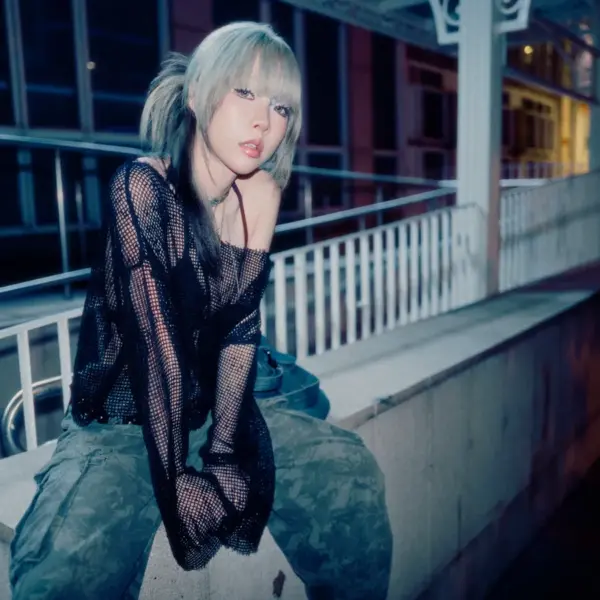 Woman sitting on a concrete ledge at night wearing a black mesh top and camo pants, styled with cool-toned lighting that reflects the Glam Guitar Trend aesthetic.
