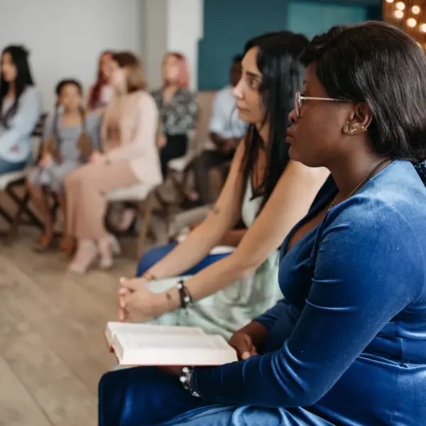 In Monday's daily devotional, a group of people are listening to Bible teaching with open Bibles in hand in a church setting.