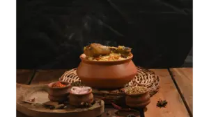 A steaming clay pot filled with rice and chicken sits on a wooden table surrounded by spices and small earthen bowls, capturing the rustic essence of ancient food and traditional cooking.