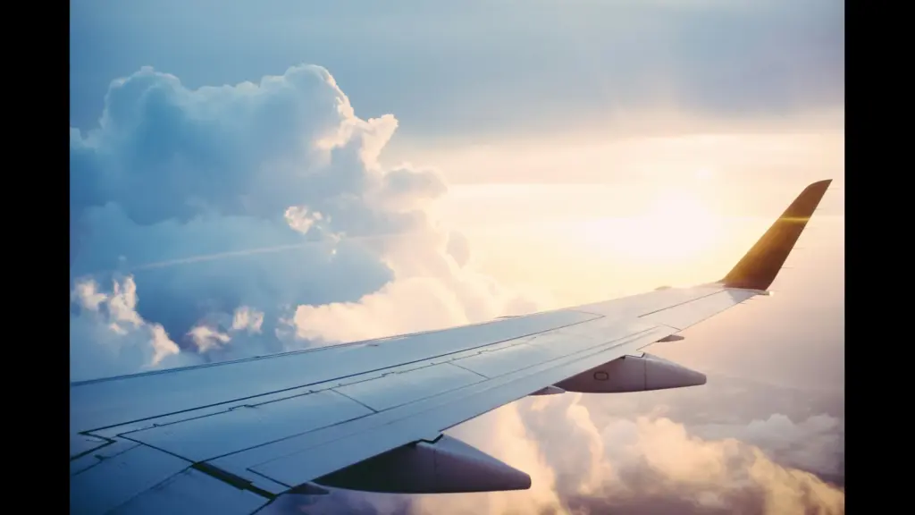 Aerial view from an airplane wing above fluffy clouds during sunset. Labor Day, travel forecast, air fare