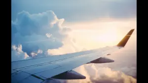 Aerial view from an airplane wing above fluffy clouds during sunset. Labor Day, travel forecast, air fare
