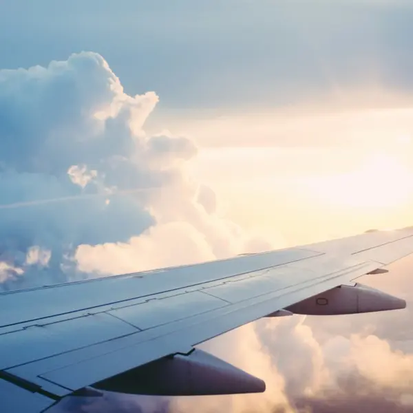 Aerial view from an airplane wing above fluffy clouds during sunset. Labor Day, travel forecast, air fare
