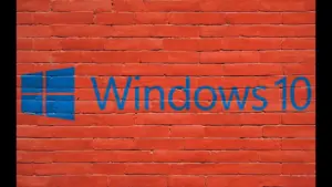 A blue Windows 10 logo and wordmark span a bright red brick wall, contrasting sleek technology branding with rough masonry in a bold, striking scene.