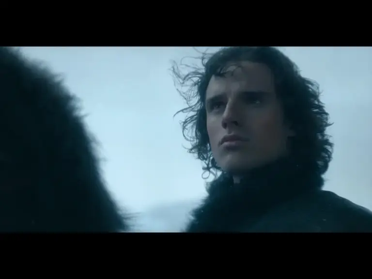 A close-up of a young man with curly hair, looking thoughtfully into the distance against a stormy sky.