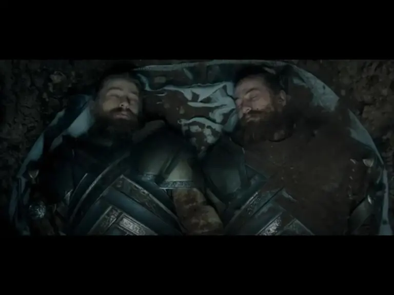 Two armored men lying side by side in a grave, covered in dirt and appearing to be deceased.