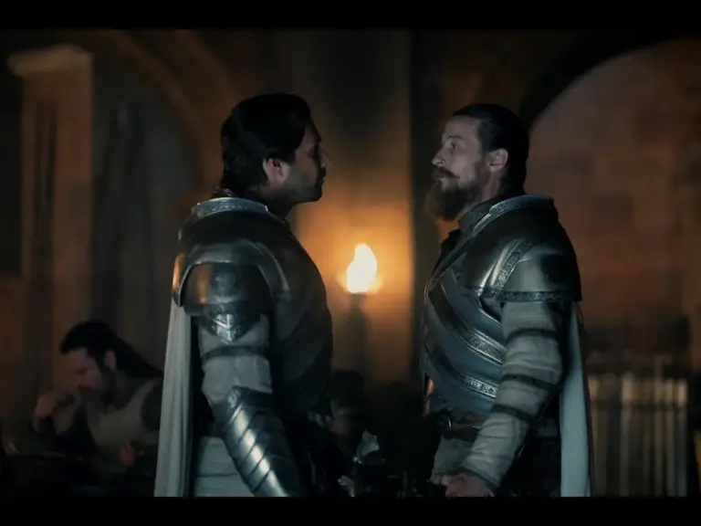 Luke Tittensor and Fabien Frankel in House of the Dragon (2022) face each other in a dimly lit room, with one appearing assertive and the other contemplative.