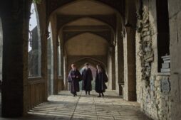 Harry Potter and the Philosopher's Stone cast, Alastair Stout, Dominic McLaughlin, and Arabella Stanton, in robes, walking through an ornate stone corridor.