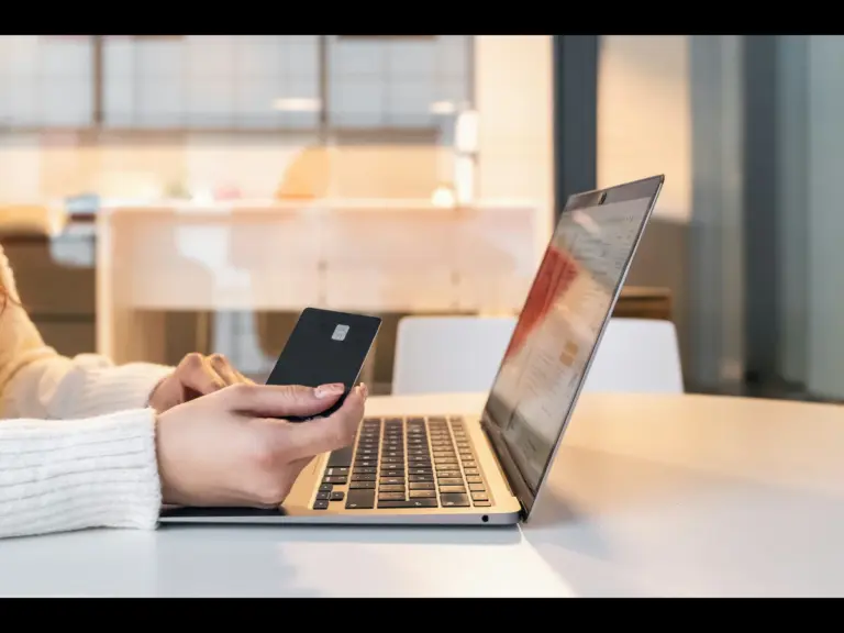 A person holding a black credit card while using a laptop on a table.