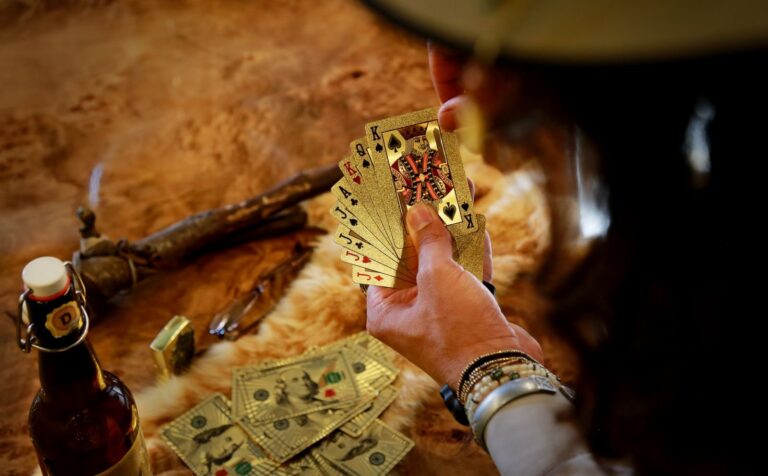 A hand holds gold playing cards over scattered cash, evoking the high-stakes deception of Liar Game season 2