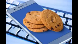 Cookies on a smartphone symbolizing data rests on a computer keyboard, displaying a stack of chocolate chip cookies against a blue screen, suggesting online food shopping or a sweet craving.