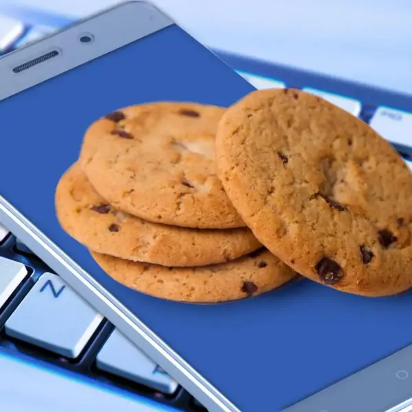 Cookies on a smartphone symbolizing data rests on a computer keyboard, displaying a stack of chocolate chip cookies against a blue screen, suggesting online food shopping or a sweet craving.