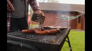 A person grilling sausages and burgers on a barbecue outside a house. Labor day. Backyard barbecue. Holiday
