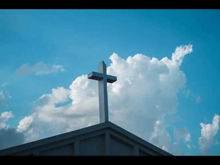In Monday's daily devotional, the top of church with a cross is seen against a cloudy blue sky.