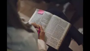 In Thursday's daily devotional, a woman studies the Bible, which has a sticky note on one side.